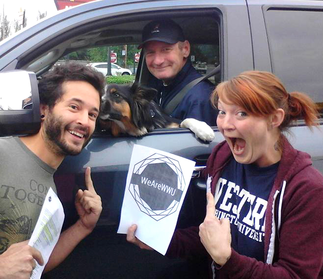 Two students posing with a man (Ryan Stiles) in a truck and his dog. One student holds a sign saying WeAreWWU