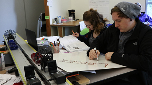 2 students working together, one writing answers on a whiteboard