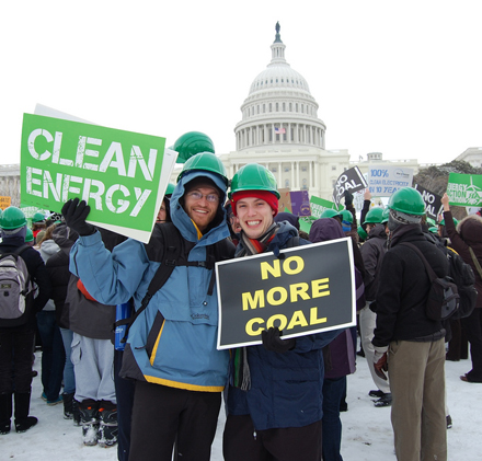 A group of protesters outside the capitol building, holding signs saying clean energy and no more coal.