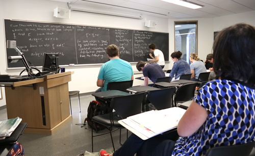 Dr. Treneer observing a student presenting a theorem on a chalkboard at the front of the class
