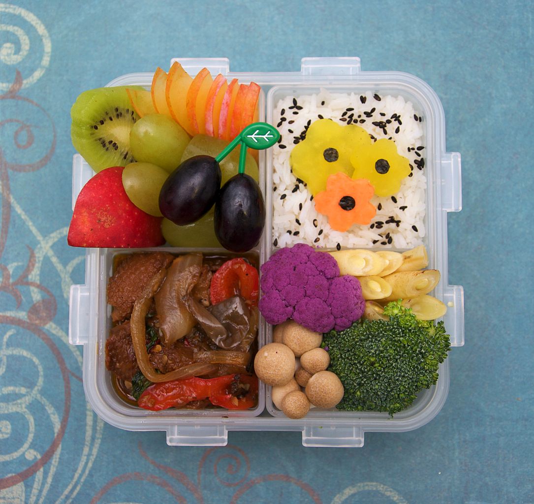 A Japanese style bento box. Contains rice, various fruits, peppers, and vegetables