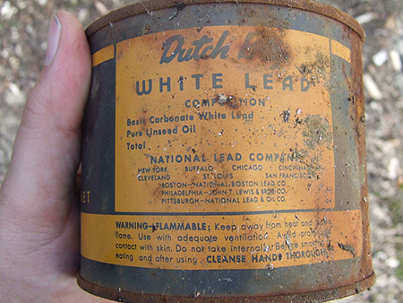 A hand holding and displaying a can of lead paint