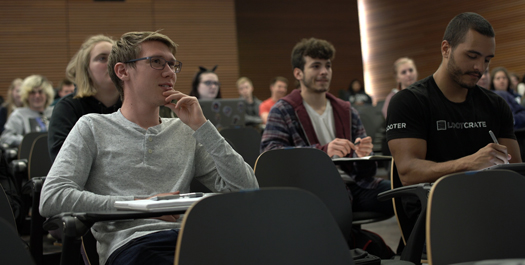 A contemplative looking student next to another student writing on an ipad