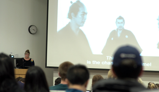 Chapman in front of a black and white movie clip of two Japanese men