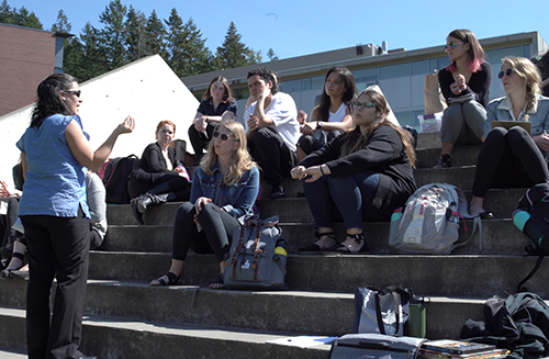 Ferreras-Stone talking to a class sitting on the scupture in front of the Comm Lawn